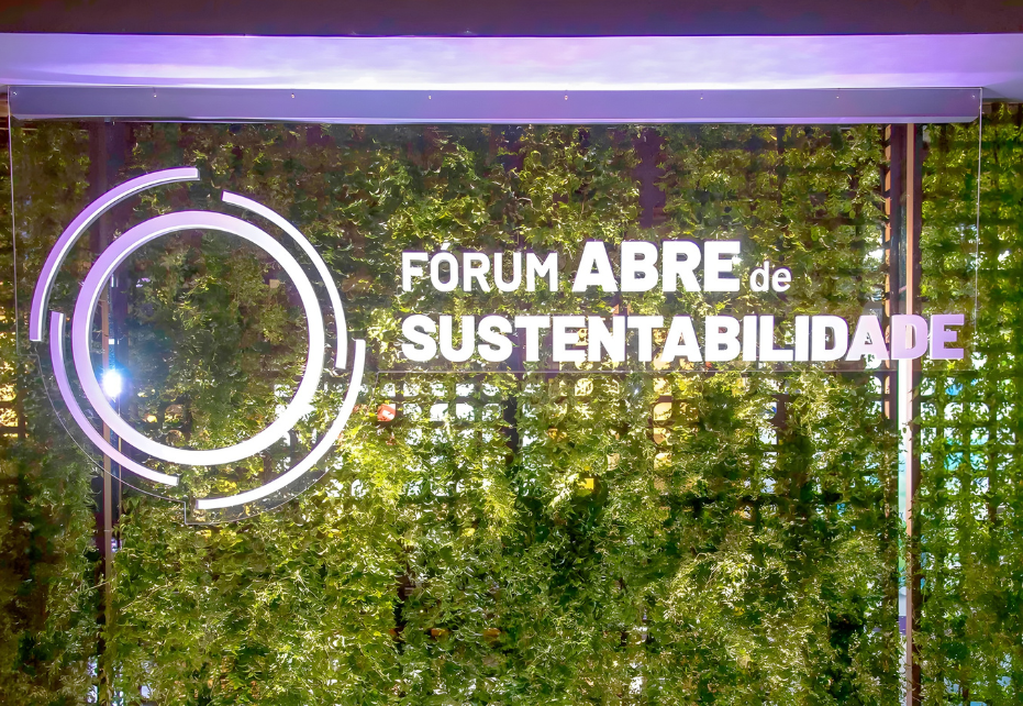 Painel do Fórum ABRE de Sustentabilidade com logo e nome do evento sobre parede verde, destacando temática ambiental.