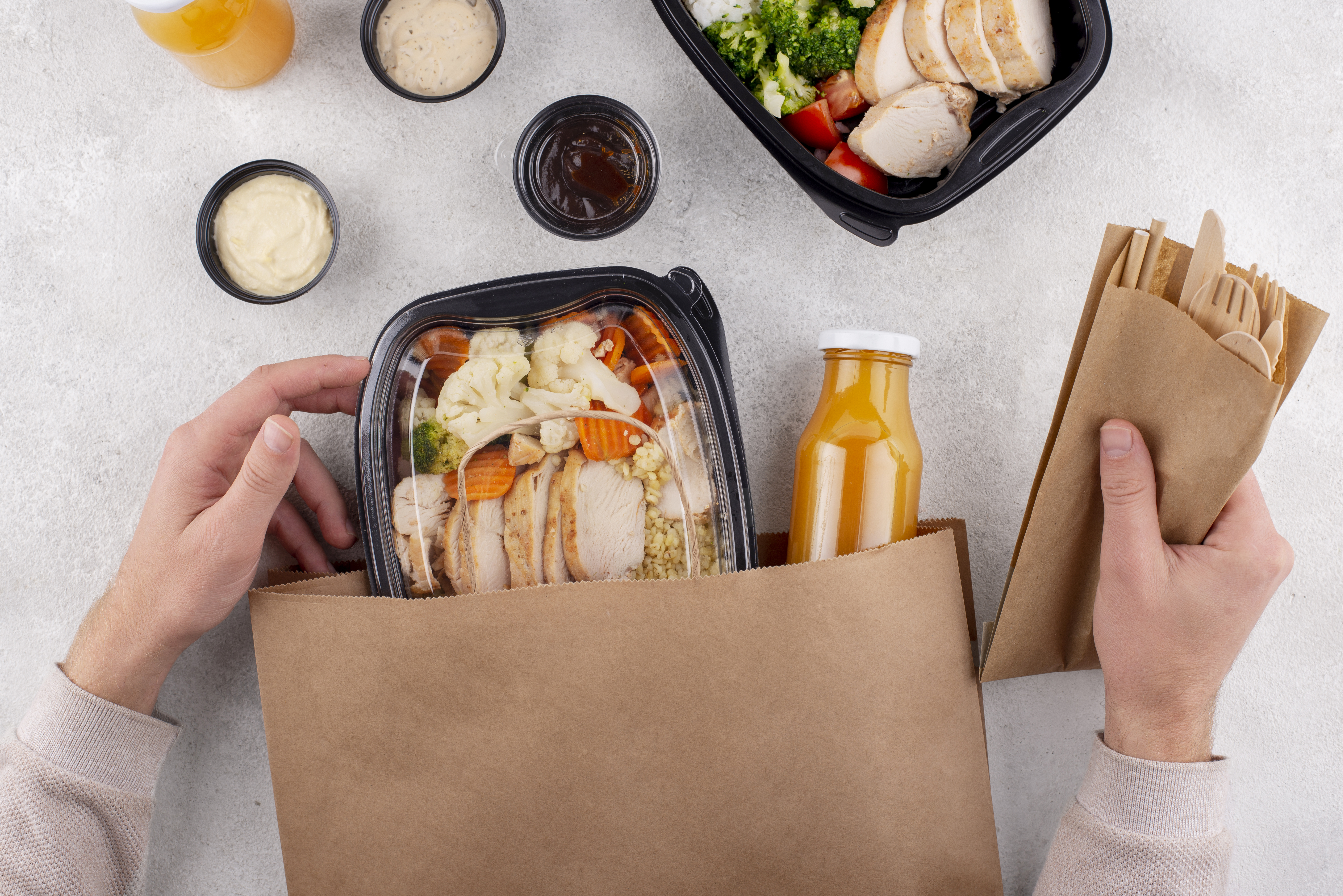 Pessoa segurando sacola de delivery com marmitas, bebida e talheres descartáveis de madeira, representando soluções práticas para alimentação e entrega sustentável.