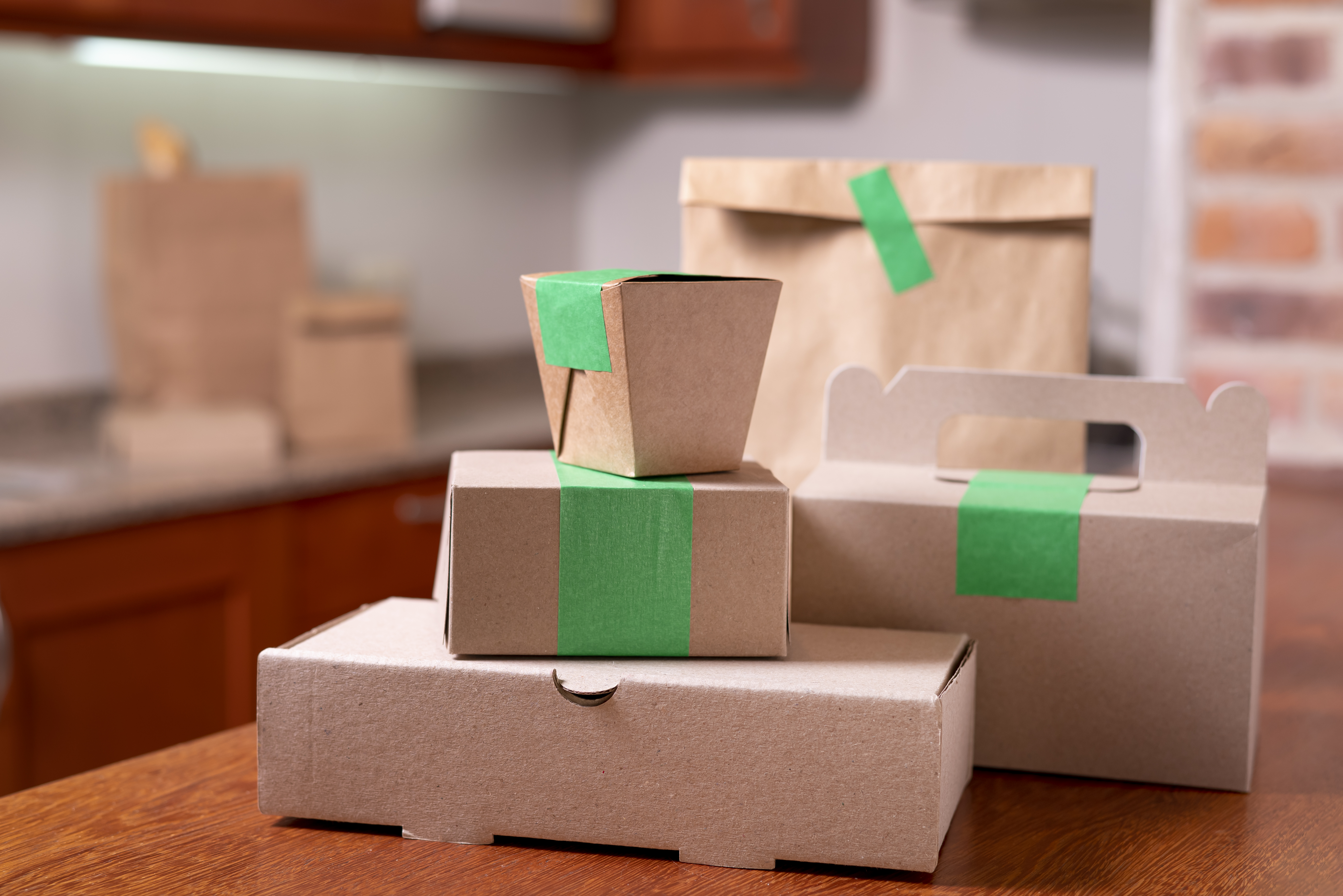 Conjunto de embalagens kraft para delivery e food service, incluindo caixas, sacolas e recipientes sustentáveis organizados sobre mesa de madeira.