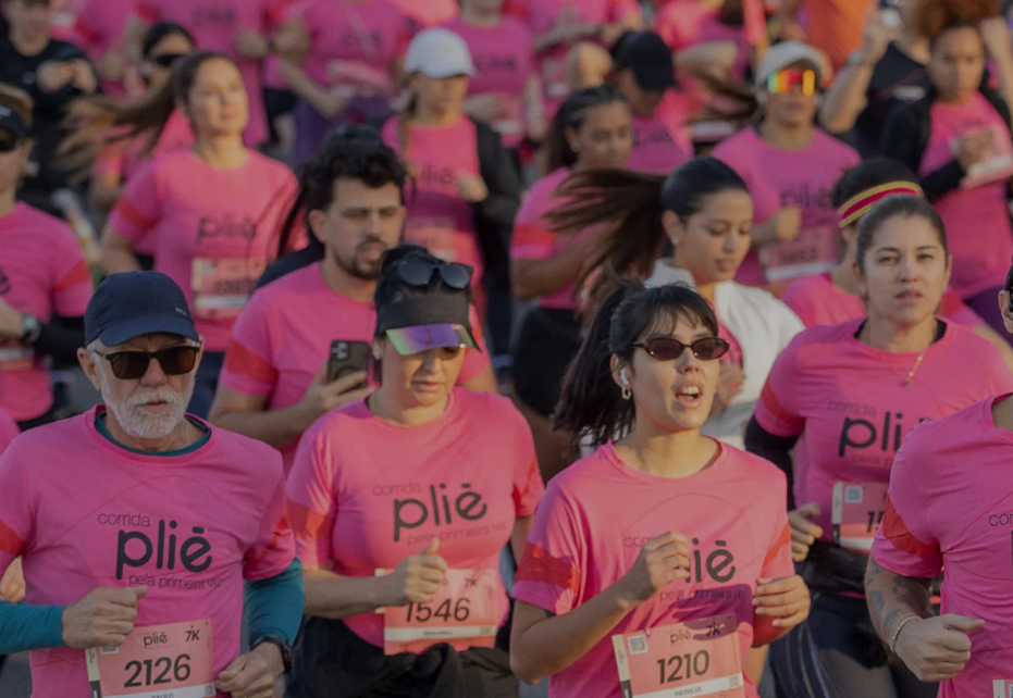 Grupo de corredores usando camisetas rosas durante corrida de rua, representando evento esportivo e promoção de saúde e bem-estar.