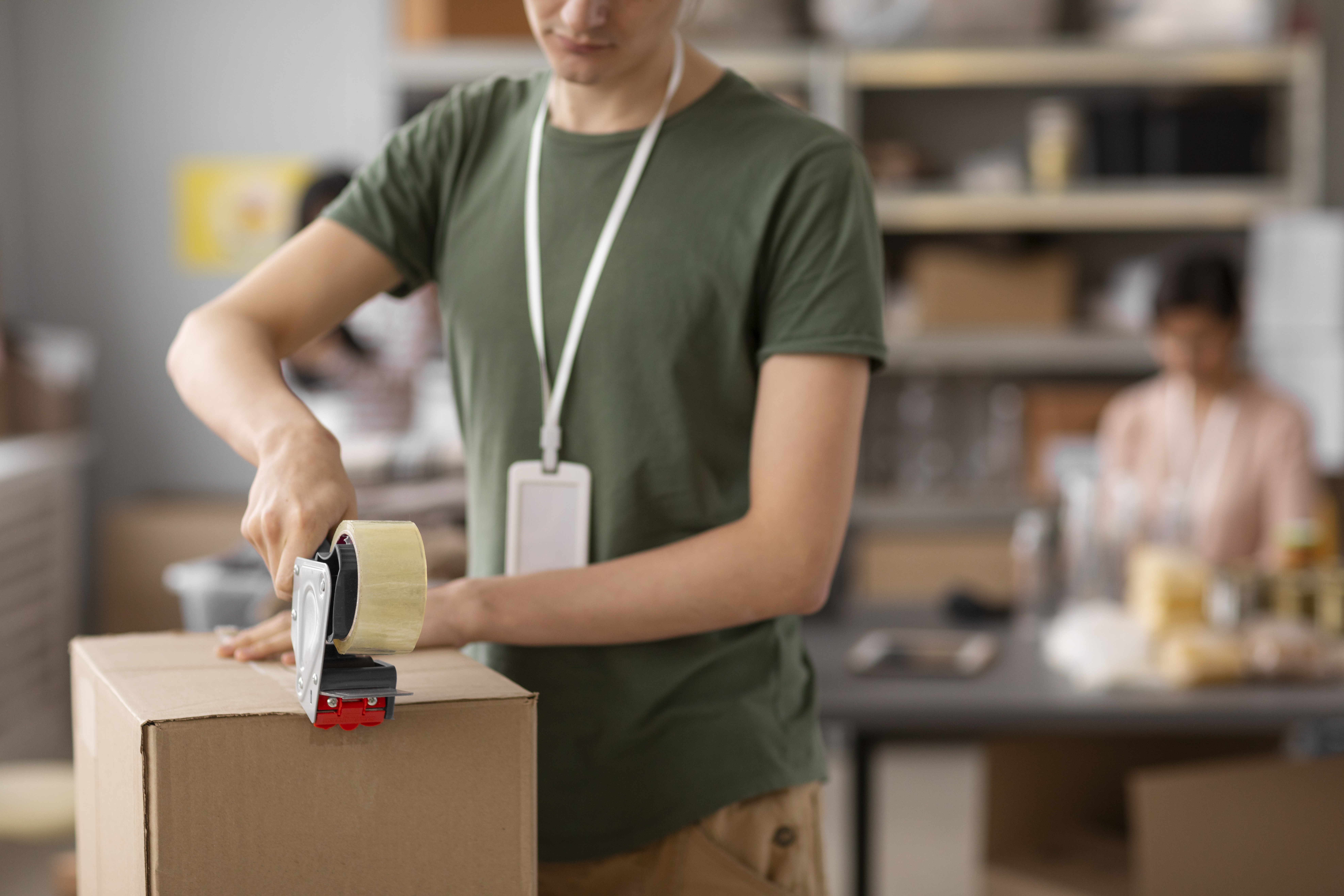 Pessoa lacrando caixa de papelão com fita adesiva, em atividade de embalagem ou preparação de doações.