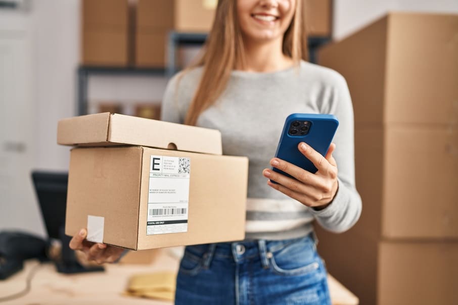 Mujer sosteniendo paquetes de eCommerce mientras revisa su celular  