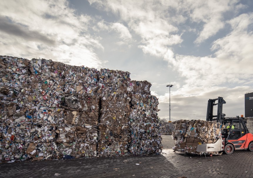 Pacas de cartón posconsumo prensado en planta de reciclaje industrial, con montacargas transportando material para su reutilización. 
